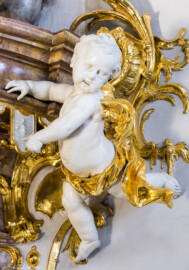 Bruchsal - Peterskirche / St. Peter - Von Innen / Von Südost - Blick auf den rechten unteren Putto am Deckel der Kanzel (Kanzel geschaffen von Johann Michael Feuchtmayer, 1756) (aufgenommen im März 2022, am Nachmittag, nach der Renovierung)
