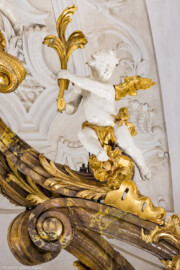 Bruchsal - Peterskirche / St. Peter - Hochaltar, oben, rechts - Blick von der Orgelempore auf den oberen rechten Putto des Hochaltars (unterhalb des Kreuzes) (Altar entworfen von Balthasar Neumann und Johann Wolfgang van der Auwera, vor 1747) (aufgenommen im März 2022, am frühen Nachmittag, nach der Renovierung)