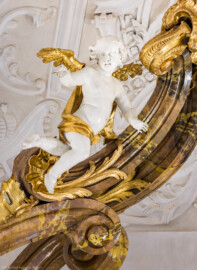 Bruchsal - Peterskirche / St. Peter - Hochaltar, oben, links - Blick von der Orgelempore auf den oberen linken Putto des Hochaltars (unterhalb des Kreuzes) (Altar entworfen von Balthasar Neumann und Johann Wolfgang van der Auwera, vor 1747) (aufgenommen im März 2022, am Nachmittag, nach der Renovierung)