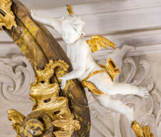 Bruchsal - Peterskirche / St. Peter - Hochaltar, oben, rechts - Blick von der Orgelempore auf den oberen rechten Putto des Hochaltars (oberhalb des Architravs) (Altar entworfen von Balthasar Neumann und Johann Wolfgang van der Auwera, vor 1747) (aufgenommen im März 2022, am Nachmittag, nach der Renovierung)