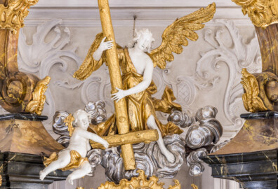 Bruchsal - Peterskirche / St. Peter - Hochaltar, Mitte, oberhalb des Altarbildes - Blick von der Orgelempore auf den Engel mit dem Petruskreuz und einen Putto (Altar entworfen von Balthasar Neumann und Johann Wolfgang van der Auwera, vor 1747) (aufgenommen im März 2022, am Nachmittag, nach der Renovierung)