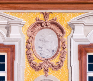 Schloss Bruchsal - Kirchenflügel / Hofkirche / St. Damian und Hugo - Von Westen - Blick vom Kavaliersbau auf die obere linke Landschaftgrisaille sowie die illusionistischen Fassadenmalerei der Westfassade der Hofkirche (ursprünglich gemalt von Giovanni Francesco Marchini, zwischen 1732 und 1737) (aufgenommen im März 2022, am Nachmittag)