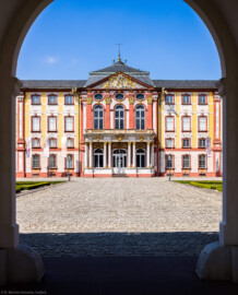 Schloss Bruchsal - Hauptbau / Corps de Logis - Von Außen - Von Osten / Hofseite - Blick vom Durchgang des Torwachtgebäudes auf die Ostfassade des Hauptbaus (aufgenommen im April 2022, am frühen Nachmittag)
