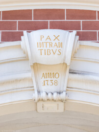 Schloss Bruchsal - Torwachtgebäude / Schlosswachthaus - Von Außen - Von Osten - Blick auf die Volute mit der Inschrift "PAX INTRAN TIBVS" (in etwa: "Friede denen, die eintreten") sowie der Jahreszahl 1738 über dem Durchgang an der Ostfassade des Torwachtgebäudes (aufgenommen im April 2022, am Nachmittag) Schloss Bruchsal - Torwachtgebäude / Schlosswachthaus - Von Außen - Von Osten - Blick auf die Volute mit der Inschrift "PAX INTRAN TIBVS" (in etwa: "Friede denen, die eintreten") sowie der Jahreszahl 1738 über dem Durchgang an der Ostfassade des Torwachtgebäudes (aufgenommen im April 2022, am Nachmittag)