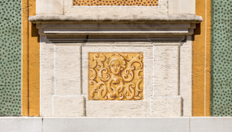 Schloss Bruchsal - Nördliche Orangerie / Nebendienstdienerbau - Von außen - Von Süden - Südfassade, links, unten - Blick auf Details der Scheinarchitektur mit einem verzierten Kopfbild (ursprünglich gemalt von Giovanni Francesco Marchini, zwischen 1732 und 1737, restauriert von Josef Mariano Kitschker, zwischen 1900 und 1910, erneut restauriert von Klaus Siller (Fassadenmalerei) und  Walter Maschke (Allegorien), 1976) (aufgenommen im April 2022, am Nachmittag)