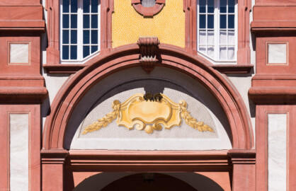Schloss Bruchsal - Südlicher Verbindungsbau - Von Osten / Hofseite - Blick vom Ehrenhof auf das Bogenfeld mit einer Kartusche oberhalb des Durchgangs zur Schlossterrasse (aufgenommen im Juli 2022, am späten Vormittag)