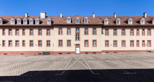 Schloss Bruchsal - Großer Dienerbau / Finanzamt - Von Außen - Mitteltrakt - Von Osten - Blick nach Westen auf die Ostfassade und den Mittelrisalit des Mitteltrakts; in der Mitte der Durchgang zur Schönbornstraße (aufgenommen im Juli 2022, um die Mittagszeit) Schloss Bruchsal - Großer Dienerbau / Finanzamt - Von Außen - Mitteltrakt - Von Osten - Blick nach Westen auf die Ostfassade und den Mittelrisalit des Mitteltrakts; in der Mitte der Durchgang zur Schönbornstraße (aufgenommen im Juli 2022, um die Mittagszeit)
