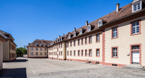 Schloss Bruchsal - Großer Dienerbau / Finanzamt - Von Außen - Mitteltrakt und Südlicher Flügel - Von Nordosten - Blick nach Südwesten auf die Ostfassade des Mitteltrakts (rechts) sowie die Nordseite des südlichen Flügels (Mitte), links zwei der drei kleinen rückwärtigen Häuser (aufgenommen im Juli 2022, um die Mittagszeit)