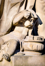 Schloss Bruchsal - Garten - Hauptachse, Südseite, 2. Skulptur von Osten - Kindliche Figur (links unten) der Skulptur "Der Winter" aus dem Skulpturenensemble "Vier Jahreszeiten" (Kopie; Original gehauen 1759 von Joachim Günther, befindet sich im Harvard Art Museum / Fogg Museum) (aufgenommen im Juli 2022, am Vormittag)