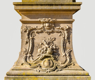 Schloss Bruchsal - Schlossgarten - Hauptachse, Südseite, 4. Skulptur von Osten - Nordseite / Frontseite des Sockels der Skulptur "Die Erde" aus dem Skulpturenensemble "Vier Elemente" (Kopie; Original gehauen 1761 von Joachim Günther, befindet sich im Gartensaal des Hauptbaus) (aufgenommen im Juli 2022, am Vormittag)