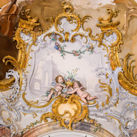 Schloss Bruchsal - Hauptbau / Corps de Logis - Beletage - Marmorsaal / Kaisersaal - Nordostecke, oben, Stuckfeld - Von Südwesten - Blick auf zwei Putti (als allegorische Darstellung des Frühlings) sowie auf umgebende Rokoko-Stuckaturen (Stuckaturen ursprünglich von Johann Michael Feichtmayr) (aufgenommen im August 2022, um die Mittagszeit) Schloss Bruchsal - Hauptbau / Corps de Logis - Beletage - Marmorsaal / Kaisersaal - Nordostecke, oben, Stuckfeld - Von Südwesten - Blick auf zwei Putti (als allegorische Darstellung des Frühlings) sowie auf umgebende Rokoko-Stuckaturen (Stuckaturen ursprünglich von Johann Michael Feichtmayr) (aufgenommen im August 2022, um die Mittagszeit)