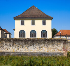 Bad Schönborn / Bad Mingolsheim - Schloss Kislau - Küchenbau / Hauptbau / Kavalierbau - Von Osten - Blick vom Landgraben auf die Ostfassade des Küchenbaus sowie auf die originale Umgebungsmauer; links der Hauptbau, rechts der Kavalierbau (aufgenommen im August 2022, am späten Vormittag)