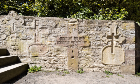 Bruchsal - Peterskirche / St. Peter - Treppenaufgang zum Friedhof, südlich des Chors - Von Außen - Von Osten - Blick auf ein Steinkreuz, evtl. ein Pestkreuz (Höhe 117 cm, Breite 84 cm; gotische Minuskel; Inschrift: "1514 / Bittent gott fur luft / geschlecht vnd fur die / arme(n) sel/"; kein direkter Hinweis auf eine Anrufung Gottes in Pestgefahr oder auf eine 1514 herrschende Epidemie; siehe www.inschriften.net, https://nbn-resolving.de/urn:nbn:de:0238-di020h007k0014206) (aufgenommen im August 2022, am frühen Nachmittag)
