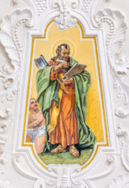 Bruchsal - Peterskirche / St. Peter - Kuppel, Apostelfiguren - Blick auf das Bildnis des Apostels und Evangelisten Matthäus; dargestellt mit einem Evangelienbuch, einem Engel als Evangelisten-Symbol sowie einem Henkersbeil (Matthäus soll unter dem Henkersbeil gestorben sein); auf dem Buchdeckel ist zu lesen: „Gemalt von Jos. Mariano Kitschker aus München 6. Juni MCMVII„ (gemalt von Josef Mariano Kitschker, zwischen 1907 und 1909) (aufgenommen im August 2022, am Nachmittag, nach der Renovierung)