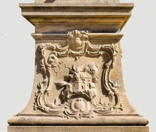 Schloss Bruchsal - Schlossgarten - Hauptachse, Nordseite, 4. Skulptur von Osten - Südseite / Frontseite des Sockels der Skulptur "Das Feuer" aus dem Skulpturenensemble "Vier Elemente" (Kopie; Original gehauen 1761 von Joachim Günther, befindet sich im Gartensaal des Hauptbaus) (aufgenommen im August 2022, am späten Vormittag)