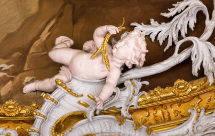 Schloss Bruchsal - Hauptbau / Corps de Logis - Beletage - Marmorsaal / Kaisersaal - Stuckaturzone im unterern Teil der Decke, oberhalb der nordöstlichen Doppelsäule - Blick auf einen Putto (Stuck urspünglich von Johann Michael Feuchtmayer dem Jüngeren, rekonstruiert 1962 bis 1969 von Jakob und Josef Schnitzer) (aufgenommen im Februar 2023, am Nachmittag)