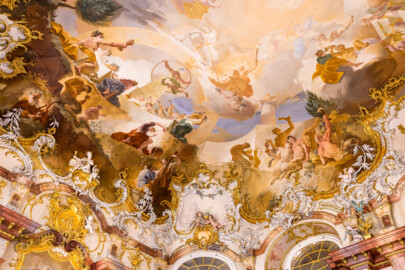 Schloss Bruchsal - Hauptbau / Corps de Logis - Von innen - Beletage - Marmorsaal / Kaisersaal - Decke, nordöstliches Viertel - Von Südwesten - Blick nach oben auf die nordöstliche Ecke der Decke - Links: das ewige Göttermahl (mit Posaunenbläsern) im Olymp als Symbol für das ewige Bestehen des Bistum Speyer; links der Mitte: der Weltbaumeister Demogorgon mit Schlangenring als Symbol der Ewigkeit, vor einem Obelisk mit einer Weltkugel oben; rechts der Mitte: der Sonnengott Apoll mit seinem Sonnenwagen über dem  Zodiacus (dem Tierkreis); unterhalb des Sonnenwagens: zwei Horen, Göttinnen der Jahreszeiten, Tau aus Krügen gießend; rechts oben: Darstellung der Fruchtbarkeitsgöttin Ceres / Demeter mit Blütenkranz und einem Begleiter mit dem Füllhorn; darunter: Darstellung des Wasser-/Meeresgotts Neptun / Poseidon mit seinem Dreizack; rechts unten: Darstellung betrunkener Satyrn mit Weinkelchen (Deckenfresko urspünglich gemalt 1754 von Johannes Zick, originalgetreu rekonstruiert 1971 bis 1974 von Wolfram Köberl; Stuck urspünglich von Johann Michael Feuchtmayer dem Jüngeren, rekonstruiert 1962 bis 1969 von Jakob und Josef Schnitzer) (aufgenommen im März 2023, am frühen Nachmittag)