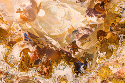 Schloss Bruchsal - Hauptbau / Corps de Logis - Von innen - Beletage - Marmorsaal / Kaisersaal - Decke, südöstliches Viertel - Von Nordwestem - Blick nach oben auf die südöstliche Ecke der Decke - Links ganz oben: Darstellung der Göttin der Jagd Diana / Artemis, mit Pfeil und Bogen und einer Mondsichel auf dem Kopf; darunter auf einer Wolke: ein Mädchen mit einem Korb mit Früchten und ein junger Mann als Staffagefigur; rechts mittig: Darstellung der drei Parzen, der drei Schicksalsgöttinnen; ein Putto macht die Schere zum Durchschneiden des Schicksalsfadens unbrauchbar; darunter: Darstellung des Herakles / Hercules sowie der Glücksgöttin Fortuna / Tyche, mit Flügeln, die ein Putto stutzt; Mitte und rechts: Darstellung einer Scheinarchitektur und des Ewigen Herdfeuers im Tempel der Vesta (Deckenfresko urspünglich gemalt 1754 von Johannes Zick, originalgetreu rekonstruiert 1971 bis 1974 von Wolfram Köberl; Stuck urspünglich von Johann Michael Feuchtmayer dem Jüngeren, rekonstruiert 1962 bis 1969 von Jakob und Josef Schnitzer) (aufgenommen im März 2023, am frühen Nachmittag) Schloss Bruchsal - Hauptbau / Corps de Logis - Von innen - Beletage - Marmorsaal / Kaisersaal - Decke, südöstliches Viertel - Von Nordwestem - Blick nach oben auf die südöstliche Ecke der Decke - Links ganz oben: Darstellung der Göttin der Jagd Diana / Artemis, mit Pfeil und Bogen und einer Mondsichel auf dem Kopf; darunter auf einer Wolke: ein Mädchen mit einem Korb mit Früchten und ein junger Mann als Staffagefigur; rechts mittig: Darstellung der drei Parzen, der drei Schicksalsgöttinnen; ein Putto macht die Schere zum Durchschneiden des Schicksalsfadens unbrauchbar; darunter: Darstellung des Herakles / Hercules sowie der Glücksgöttin Fortuna / Tyche, mit Flügeln, die ein Putto stutzt; Mitte und rechts: Darstellung einer Scheinarchitektur und des Ewigen Herdfeuers im Tempel der Vesta (Deckenfresko urspünglich gemalt 1754 von Johannes Zick, originalgetreu rekonstruiert 1971 bis 1974 von Wolfram Köberl; Stuck urspünglich von Johann Michael Feuchtmayer dem Jüngeren, rekonstruiert 1962 bis 1969 von Jakob und Josef Schnitzer) (aufgenommen im März 2023, am frühen Nachmittag)