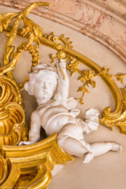 Schloss Bruchsal - Hauptbau / Corps de Logis - Beletage - Marmorsaal / Kaisersaal - Südwand, oberstes Gesims - Blick auf einen Putto rechts der Mitte (Stuck urspünglich von Johann Michael Feuchtmayer dem Jüngeren, rekonstruiert 1962 bis 1969 von Jakob und Josef Schnitzer) (aufgenommen im März 2023, am Nachmittag)