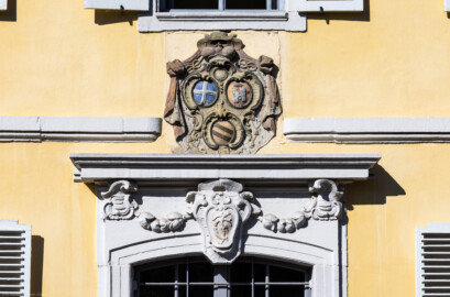 Bad Schönborn / Bad Mingolsheim - Schloss Kislau - Kavalierbau, Mitte, über der zentralen östlichen Tür - Von Osten - Blick auf das Allianzwappen von Franz Christoph von Hutten zum Stolzenberg (unten: Wappen des Fürstbischofs Franz Christoph, links: Wappen des Hochstifts Speyer, rechts: Wappen der Propstei Weißenburg) sowie auf das Monogram ("FC") von Franz Christoph (aufgenommen im April 2023, am späten Vormittag)