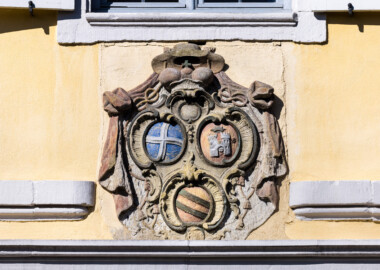 Bad Schönborn / Bad Mingolsheim - Schloss Kislau - Kavalierbau, Mitte, über der zentralen östlichen Tür - Von Osten - Blick auf das Allianzwappen von Franz Christoph von Hutten zum Stolzenberg (unten: Wappen des Fürstbischofs Franz Christoph, links: Wappen des Hochstifts Speyer, rechts: Wappen der Propstei Weißenburg) (aufgenommen im April 2023, am späten Vormittag)