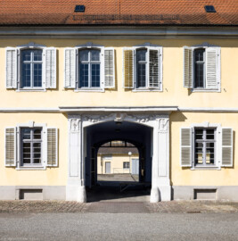 Bad Schönborn / Bad Mingolsheim - Schloss Kislau - Kavalierbau, südliche Durchfahrt - Von Osten - Blick nach Westen auf das Portal der südlichen Durchfahrt und auf den Innenhof; im Hintergrund die Handwerkerwerkstatt (aufgenommen im April 2023, am späten Vormittag)