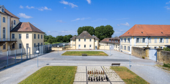 Bad Schönborn / Bad Mingolsheim - Schloss Kislau - Krankenbau / Hauptbau / Kavalierbau - Von Osten - Blick vom mittleren Fenster des 1. Obergeschosses des Küchenbaus nach Westen auf den ehemaligen Ehrenhof, den Krankenbau (ehemals Heiduckenbau bzw. Lakaienspeisehaus, in der Mitte), den Hauptbau mit dem Westflügel (links), ein Stallungsgebäude (rechts der Mitte, nach hinten), den Kavalierbau (rechts) sowie auf die alte Trennmauer zum Ehrenhof (ganz rechts) (aufgenommen im Juni 2023, am späten Vormittag)