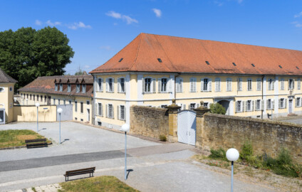 Bad Schönborn / Bad Mingolsheim - Schloss Kislau - Kavalierbau / Stallungsgebäude / Krankenbau / Tor zum Ehrenhof - Von Südost - Blick vom mittleren Fenster des 1. Obergeschosses des Küchenbaus nach Nordwest auf den ehemaligen Ehrenhof, den Kavalierbau (Mitte), ein ehemaliges Stallungsgebäude (links), den Krankenbau (ehemals Heiduckenbau bzw. Lakaienspeisehaus, ganz links) sowie auf die Trennmauer und das Tor zum Ehrenhof (aufgenommen im Juni 2023, um die Mittagszeit)