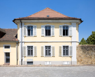 Bad Schönborn / Bad Mingolsheim - Schloss Kislau - Kavalierbau / Stallungsgebäude / Trennmauer - Von Süden - Blick vom Ehrenhof auf die Südfassade des Kavalierbaus (Mitte), ein ehemaliges Stallungsgebäude (links) sowie auf die Trennmauer zum Ehrenhof (rechts) (aufgenommen im Juni 2023, am frühen Nachmittag)