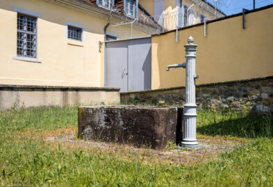 Bad Schönborn / Bad Mingolsheim - Schloss Kislau - Brunnen, nördlich und nahe dem Heiduckenbau - Von Südwesten - Blick im ehemaligen Garten (heute Sportplatz) nahe dem Heiduckenbau nach Nordosten auf einen alten Brunnen mit einer umgebauten Handpumpe (aufgenommen im Juni 2023, am Nachmittag)