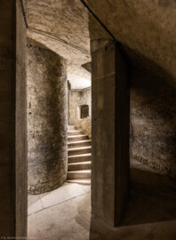 Bad Schönborn / Bad Mingolsheim - Schloss Kislau - Hauptbau - Von Innen - Treppenhaus, Keller - Blick von der Kellerwand auf das Treppenauge (der innere Zylinder vom Boden bis zur Decke, um den sich die Treppe windet) sowie den Beginn der Wendeltreppe, im Vordergrund Teile des die Treppe umfassenden Zylinders mit Öffnungen vom Boden bis zur Decke (aufgenommen im Mai 2024, am Nachmittag)
