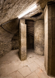Bad Schönborn / Bad Mingolsheim - Schloss Kislau - Hauptbau - Von Innen - Treppenhaus, Keller - Blick von der Kellerwand auf eine Öffnung vom Boden bis zur Decke des äußeren Zylinders um die Treppe, auf Teile der Wendeltreppe (rechts davon) sowie rechts der Treppe auf das runde Treppenauge (der innere Zylinder, um den sich die Treppe windet) (aufgenommen im Mai 2024, am frühen Nachmittag)