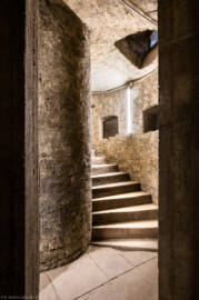 Bad Schönborn / Bad Mingolsheim - Schloss Kislau - Hauptbau - Von Innen - Treppenhaus, Keller - Blick von der Kellerwand auf das Treppenauge (der innere Zylinder vom Boden bis zur Decke, um den sich die Treppe windet) sowie den Beginn der Wendeltreppe, im Vordergrund Teile des die Treppe umfassenden Zylinders mit Öffnungen vom Boden bis zur Decke (aufgenommen im Mai 2024, am frühen Nachmittag)