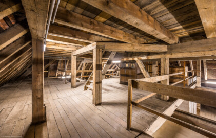 Bad Schönborn / Bad Mingolsheim - Schloss Kislau - Hauptbau - Von Innen - Dachstuhl - Obere Ebene (Ebene 3 von 4) - Von Nordwest - Blick in die obere Ebene des Dachstuhls; die Treppe (in der Bildmitte) führt in die oberste Ebene des Dachstuhls (Ebene 4 von 4) mit dem Zugang zur Turmuhr und zum Glockenturm; rechts der Treppe befindet sich der Schrank für das Uhrwerk der Turmuhr (aufgenommen im Mai 2024, am Nachmittag)