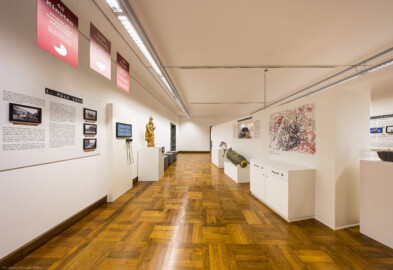 Städtisches Museum Bruchsal - Schloss Bruchsal - Hauptbau / Corps de Logis - Von innen - Westlicher Raum - "Nationalsozialismus und Zweiter Weltkrieg in Bruchsal" - Blick entlang des östlichen Gangs der Ausstellung; thematisiert sind hier: 1. März 1945 (Tag des Luftangriffs auf Bruchsal), Kriegsschäden in Bruchsal, Luftschutzobjekte aus Bruchsal; in der Bildmitte eine 500 Pfund-Sprengbombe (Raum umgestaltet und fertiggestellt in 2026) (aufgenommen im April 2026, am Nachmittag)