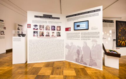 Städtisches Museum Bruchsal - Schloss Bruchsal - Hauptbau / Corps de Logis - Von innen - Westlicher Raum - "Nationalsozialismus und Zweiter Weltkrieg in Bruchsal" - Blick auf einen Teil der Westseite der Stellwände in der Mitte des Raums; auf den Stellwänden sind hier thematisiert: Massenmord an der jüdischen Bevölkerung, Deportation von Bruchsal nach Gurs,  Die Progromnacht vom 9./10. November 1938; das Gemälde illustriert den Brand der Synagoge Bruchsal (Maler: Jürgen Spatschke, Datierung: 1992, Öl auf Leinwand) (Raum umgestaltet und fertiggestellt in 2026) (aufgenommen im April 2026, am Nachmittag)