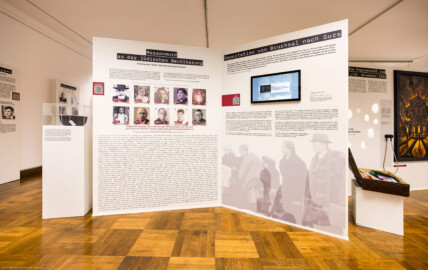 Städtisches Museum Bruchsal - Schloss Bruchsal - Hauptbau / Corps de Logis - Von innen - Westlicher Raum - "Nationalsozialismus und Zweiter Weltkrieg in Bruchsal" - Blick auf einen Teil der Westseite der Stellwände in der Mitte des Raums; auf den Stellwänden sind hier thematisiert: Massenmord an der jüdischen Bevölkerung, Deportation von Bruchsal nach Gurs,  Die Progromnacht vom 9./10. November 1938; das Gemälde illustriert den Brand der Synagoge Bruchsal (Maler: Jürgen Spatschke, Datierung: 1992, Öl auf Leinwand) (Raum umgestaltet und fertiggestellt in 2026) (aufgenommen im April 2026, am Nachmittag)