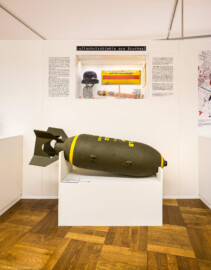 Städtisches Museum Bruchsal - Schloss Bruchsal - Hauptbau / Corps de Logis - Von innen - Westlicher Raum - "Nationalsozialismus und Zweiter Weltkrieg in Bruchsal" - Blick auf einen Teil der Ostseite der Stellwände in der Mitte des Raums; thematisiert sind hier: Luftschutzobjekte aus Bruchsal; unten eine 500 Pfund-Sprengbombe (Raum umgestaltet und fertiggestellt in 2026) (aufgenommen im April 2026, am späten Nachmittag)