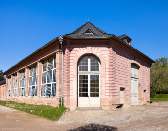 Schloss und Schlossgarten Schwetzingen - Garten - Neue Orangerie - Glashaus, Südostseite - Blick auf die südliche (links) und östliche (rechts) Fassade des nachträglich angebauten Glashauses; Glashaus nach Süden hervortretend, mit fünf großen schräg eingebauten Fenstern nach Süden und drei großen Türen nach Osten, Südosten und Südwesten (Gesamter Bau: Länge ca. 171 Meter, Breite ca. 10-12 Meter; Bauzeit: 1761-1762, Glashaus angebaut 1770; Architekt: Nicolas de Pigage; umfangreiche Instandsetzung: 1994-1999; Putzflächen bemalt in Freskotechnik, täuschen teilweise ein Scheinmauerwerk vor) (aufgenommen im April 2023, am späten Vormittag) Schloss und Schlossgarten Schwetzingen - Garten - Neue Orangerie - Glashaus, Südostseite - Blick auf die südliche (links) und östliche (rechts) Fassade des nachträglich angebauten Glashauses; Glashaus nach Süden hervortretend, mit fünf großen schräg eingebauten Fenstern nach Süden und drei großen Türen nach Osten, Südosten und Südwesten (Gesamter Bau: Länge ca. 171 Meter, Breite ca. 10-12 Meter; Bauzeit: 1761-1762, Glashaus angebaut 1770; Architekt: Nicolas de Pigage; umfangreiche Instandsetzung: 1994-1999; Putzflächen bemalt in Freskotechnik, täuschen teilweise ein Scheinmauerwerk vor) (aufgenommen im April 2023, am späten Vormittag)