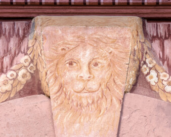 Schloss und Schlossgarten Schwetzingen - Garten - Neue Orangerie - Südseite, Mittelbau, Portal - Blick auf die Löwenmaske mit Fruchtgehängen im Schlussstein des Rundbogens (Gesamter Bau: Länge ca. 171 Meter, Breite ca. 10-12 Meter; Bauzeit: 1761-1762; Architekt: Nicolas de Pigage; umfangreiche Instandsetzung: 1994-1999; Putzflächen bemalt in Freskotechnik, täuschen teilweise ein Scheinmauerwerk vor) (aufgenommen im April 2023, am frühen Nachmittag) Schloss und Schlossgarten Schwetzingen - Garten - Neue Orangerie - Südseite, Mittelbau, Portal - Blick auf die Löwenmaske mit Fruchtgehängen im Schlussstein des Rundbogens (Gesamter Bau: Länge ca. 171 Meter, Breite ca. 10-12 Meter; Bauzeit: 1761-1762; Architekt: Nicolas de Pigage; umfangreiche Instandsetzung: 1994-1999; Putzflächen bemalt in Freskotechnik, täuschen teilweise ein Scheinmauerwerk vor) (aufgenommen im April 2023, am frühen Nachmittag)