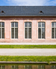 Schloss und Schlossgarten Schwetzingen - Garten - Neue Orangerie - Südseite, rechter / östlicher Seitenflügel - Blick vom Orangeriegarten auf einige Fenster des dreizehnachsigen Seitenflügels (Gesamter Bau: Länge ca. 171 Meter, Breite ca. 10-12 Meter; Bauzeit: 1761-1762; Architekt: Nicolas de Pigage; umfangreiche Instandsetzung: 1994-1999; Putzflächen bemalt in Freskotechnik, täuschen teilweise ein Scheinmauerwerk vor) (aufgenommen im Mai 2023, am späten Vormittag)