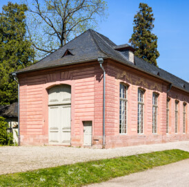 Schloss und Schlossgarten Schwetzingen - Garten - Neue Orangerie - Westseite, Eckpavillon - Von Südwest - Blick auf die Westfassade (links) und Südfassade (rechts) des Eckpavillons mit der hohen Tür (Gesamter Bau: Länge ca. 171 Meter, Breite ca. 10-12 Meter; Bauzeit: 1761-1762; Architekt: Nicolas de Pigage; umfangreiche Instandsetzung: 1994-1999; Putzflächen bemalt in Freskotechnik, täuschen teilweise ein Scheinmauerwerk vor) (aufgenommen im Mai 2023, am Nachmittag) Schloss und Schlossgarten Schwetzingen - Garten - Neue Orangerie - Westseite, Eckpavillon - Von Südwest - Blick auf die Westfassade (links) und Südfassade (rechts) des Eckpavillons mit der hohen Tür (Gesamter Bau: Länge ca. 171 Meter, Breite ca. 10-12 Meter; Bauzeit: 1761-1762; Architekt: Nicolas de Pigage; umfangreiche Instandsetzung: 1994-1999; Putzflächen bemalt in Freskotechnik, täuschen teilweise ein Scheinmauerwerk vor) (aufgenommen im Mai 2023, am Nachmittag)