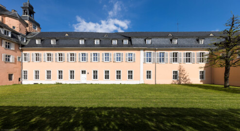 Schloss und Schlossgarten Schwetzingen - Schloss - Südflügel / Hofdamenflügel / Küchenflügel - Von Westen - Blick auf die Westfassaden des Südflügels und des Küchenflügels; die fünf linken unteren Fenster und die Tür gehören zum Querbau des Südflügels, die nächsten vier Fenster bis zum Pilaster gehören zum Längsbau des Südflügels, die drei Fenster ganz rechts gehören zum Querbau des Küchenflügels; ganz links die Südwand des Mittelbaus mit dem Südturm, ganz rechts die Nordwand des Verbindungsbaus vom Küchenflügel zum Südlichen Zirkelbau (Südflügel: L-förmig, Länge x Breite Längsbau ca. 50 x 14 Meter, Querbau ca. 15 x 11 Meter; Architekt: Johann Adam Breunig (1660-1727); Fertigstellung: 1710, letzte Renovierung: 2009-2012; Küchenflügel: L-förmig, Länge x Breite Längsbau ca. 75 x 13 Meter, Querbau ca. 25 x 11 Meter; Architekt: Nicolas de Pigage (1723-1796); Fertigstellung: 1761, letzte Renovierung: 2009-2012) (aufgenommen im Mai 2023, am späten Nachmittag)