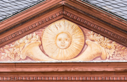 Schloss und Schlossgarten Schwetzingen - Garten - Neue Orangerie - Südseite, Mittelbau, Giebel - Blick auf den Dreiecksgiebel mit dem Sonnengesicht und den zwei Füllhörnern (Gesamter Bau: Länge ca. 171 Meter, Breite ca. 10-12 Meter; Bauzeit: 1761-1762; Architekt: Nicolas de Pigage; umfangreiche Instandsetzung: 1994-1999; Putzflächen bemalt in Freskotechnik, täuschen teilweise ein Scheinmauerwerk vor) (aufgenommen im Mai 2023, am späten Vormittag) Schloss und Schlossgarten Schwetzingen - Garten - Neue Orangerie - Südseite, Mittelbau, Giebel - Blick auf den Dreiecksgiebel mit dem Sonnengesicht und den zwei Füllhörnern (Gesamter Bau: Länge ca. 171 Meter, Breite ca. 10-12 Meter; Bauzeit: 1761-1762; Architekt: Nicolas de Pigage; umfangreiche Instandsetzung: 1994-1999; Putzflächen bemalt in Freskotechnik, täuschen teilweise ein Scheinmauerwerk vor) (aufgenommen im Mai 2023, am späten Vormittag)