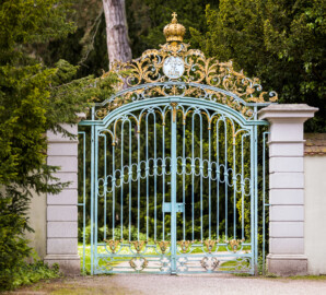 Schloss und Schlossgarten Schwetzingen - Garten - Arboretum, östliches Tor - Von Osten - Blick auf das schmiedeeiserne, teilvergoldete Prachttor mit Krone, der östliche Eingang zum Arboretum (Tor fertiggestellt 1755; entworfen von Franz Wilhelm Rabaliatti, geschmiedet von den Mannheimer Schlossermeistern Strickling und Frockmann; ursprünglich an einem anderen Ort verbaut; Schild "Arboretum" nachträglich angebracht) (aufgenommen im Mai 2023, am frühen Nachmittag)