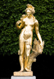 Schloss und Schlossgarten Schwetzingen - Garten - Schlossterrasse, zwischen Mittelbau und nördlichem Zirkelbau - Von Westen - Blick auf die Skulptur der Arkadischen Atalante, einer Jägerin aus Arkadien, mit einem Eber an der linken Seite (Kopie, erstellt 1972 von Hans Volker Dursy) (Bildhauer: Heinrich Charrasky (1656–1710); Datierung: wohl nach 1707; Anlehnung an eine Skulptur von Gabriel Grupello (1644-1730); Skulptur ist Teil einer Zweiergruppe auf der Schlossterrasse; Material: Blei; Fassung: Gold; die Skulptur hielt in der rechten Hand einen Speer) (aufgenommen im Mai 2023, am frühen Abend)