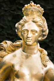 Schloss und Schlossgarten Schwetzingen - Garten - Schlossterrasse, zwischen Mittelbau und nördlichem Zirkelbau - Von Westen - Blick auf einen Teil der Skulptur der Arkadischen Atalante, einer Jägerin aus Arkadien, mit einem Eber an der linken Seite (Kopie, erstellt 1972 von Hans Volker Dursy) (Bildhauer: Heinrich Charrasky (1656–1710); Datierung: wohl nach 1707; Anlehnung an eine Skulptur von Gabriel Grupello (1644-1730); Skulptur ist Teil einer Zweiergruppe auf der Schlossterrasse; Material: Blei; Fassung: Gold; die Skulptur hielt in der rechten Hand einen Speer) (aufgenommen im Mai 2023, am frühen Abend)