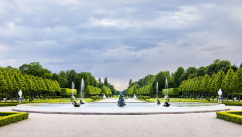 Schloss und Schlossgarten Schwetzingen - Garten - Hauptachse Ost-West / Kreisparterre - Von Osten - Blick nach Westen auf den Arionbrunnen, entlang der Ost-West-Achse, im Hintergrund die Pfalz mit dem 670 Meter hohen Kalamit (aufgenommen im Mai 2023, am frühen Abend)