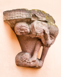 Schloss und Schlossgarten Schwetzingen - Schloss - Mittelbau - Hofseite - Von Südost - Blick auf die Spottfigur rechts des Bogens der Durchfahrt zum Garten; Datierung um 1470/80; Figur vermutlich ehemals als Säulenfuß genutzt; als Groteske streckt die Figur dem Betrachter sein Gesäß zum Spott entgegen (aufgenommen im Mai 2023, um die Mittagszeit) Schloss und Schlossgarten Schwetzingen - Schloss - Mittelbau - Hofseite - Von Südost - Blick auf die Spottfigur rechts des Bogens der Durchfahrt zum Garten; Datierung um 1470/80; Figur vermutlich ehemals als Säulenfuß genutzt; als Groteske streckt die Figur dem Betrachter sein Gesäß zum Spott entgegen (aufgenommen im Mai 2023, um die Mittagszeit)