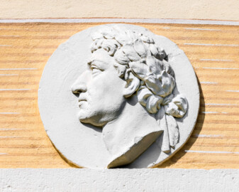 Schloss und Schlossgarten Schwetzingen - Garten - Badhaus - Von aussen - Ostseite - Medaillon oben rechts - Von Osten - Blick auf ein Feld mit einem Relief-Medaillon; dargestellt ist der Kopf von Carl Theodor (1724-1799, reg. 1742-1799), im Linksprofil, Lorbeerkranz mit Schleife im gelockten Haar; Vorbild der Darstellung ist eine Münze der Münchner Münzsammlung von Carl Theodor (Bildhauer: Franz Conrad Linck (1730-1793), Datierung: 1770-1773; Kopie, Verbleib Original unklar; Material: Terrakotta; Durchmesser: ca. 40cm) (Gesamter Bau: Länge x Breite ca. 18 x 14 Meter, Höhe ca. 10 Meter; Architekt: Nicolas de Pigage (1723-1796); Bauzeit: 1768-1772; Gesamtinstandsetzung innen und außen: 1999-2006) (aufgenommen im Mai 2023, am späten Vormittag)